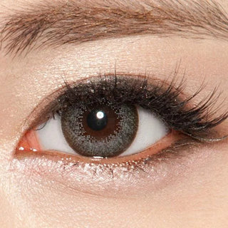 A close-up of an eye with brown irises wearing NEO Vision Extra Dali Grey lenses by NEO Vision, featuring long curled lashes and shimmery eyeshadow.