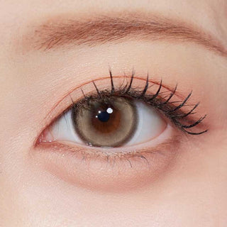 Olala Glint Brown color contact lens on top of a dark eye paired with subtle peach eyeshadow and curled wispy eyelashes