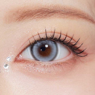 Olala Glint Grey color contact lens on top of a dark eye paired with subtle peach eyeshadow and curled wispy eyelashes.