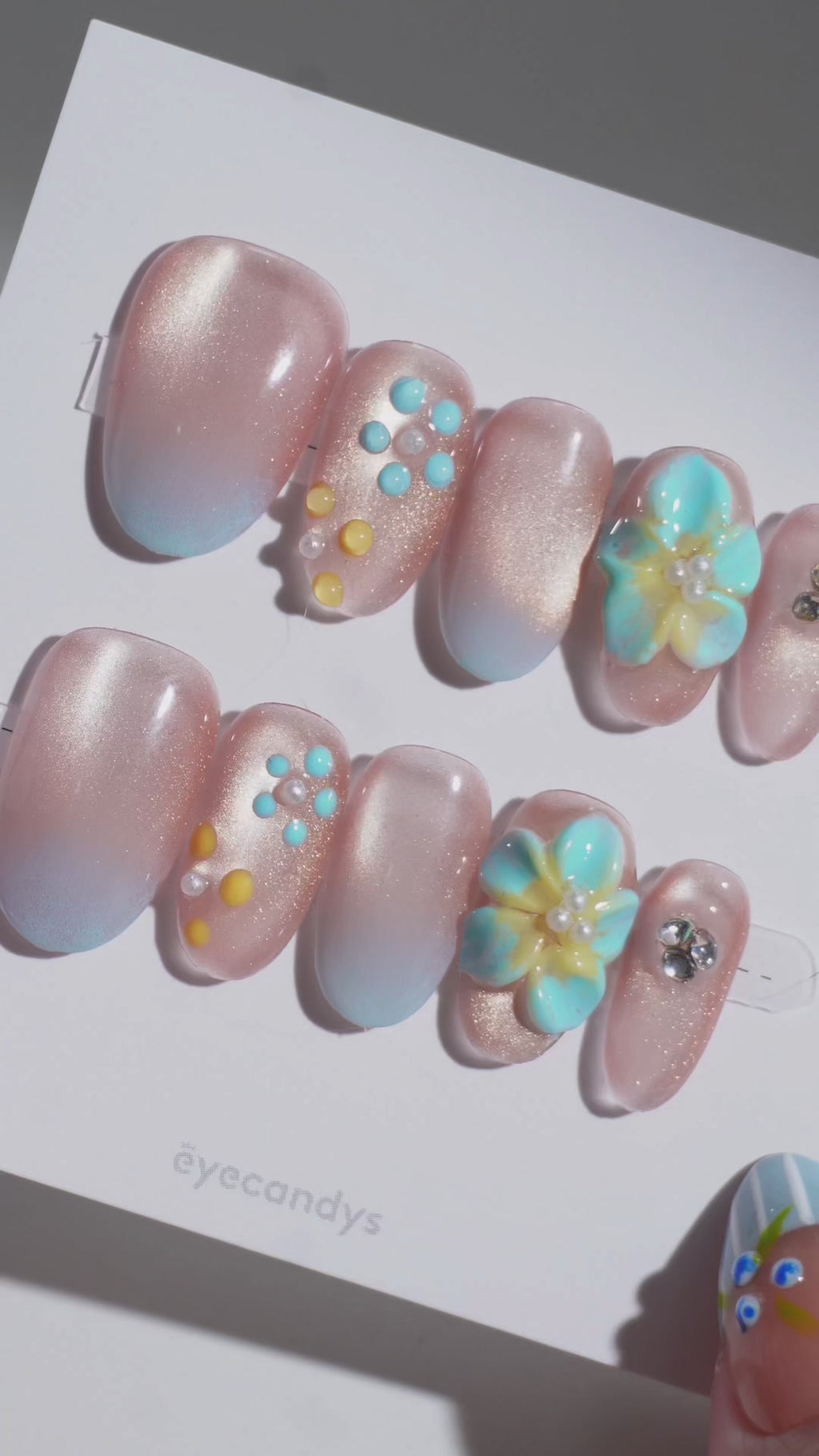 EyeCandys Lei'd Back handmade press on nails featuring a sheer nude to baby blue ombré gradient with soft gold shimmer, hand-sculpted 3D plumeria flowers in blue, yellow, and white, pearl bead centers, and crystal accents on almond-shaped nails. Tropical beach-inspired salon gel press on nails perfect for vacation nails, Hawaii-inspired nails, floral nail designs, summer nails, July nail ideas, simple 4th of July nails, coastal aesthetic, reusable handmade press on nails, and luxury nail inspiration.