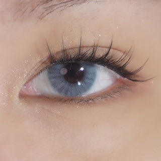 Close-up of an eye wearing EyeCandys Glossy Blue prescription colored contact lenses and Hasom First Touch Luxury 02 pre-glued lash clusters, featuring a defined manga-inspired eye look with long, nearly uniform lashes.