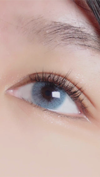Model applying the EyeCandys Glossy Blue colored contact lens with prescription, using the silicone-tipped lens applicator tool, onto her naturally dark eye