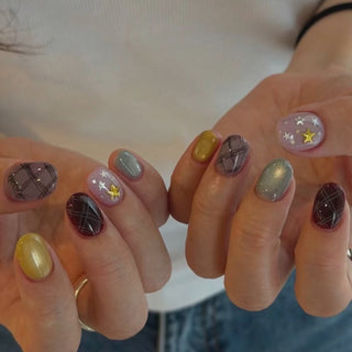 Video alt text: Hand wearing EyeCandys Show and Tell press on nails in a short squoval shape, featuring pale lavender pearl nails with silver stars and a gold star charm, chocolate brown and lavender plaid nails, a pale blue cat-eye magnetic nail, and a butter yellow accent nail, catching the light as the hand moves.