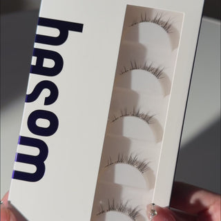 Unboxing video of EyeCandys Hasom First Touch Fancy 03 pre-glued strip lashes, showcasing the lash packaging and wispy, tapered design with a soft foxy lift at the outer corners.