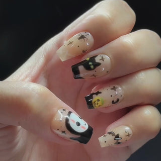 Hand wearing EyeCandys Trick or Chic Press-On Nails with warm tan nails, black drip tips, Halloween characters, and spider web details