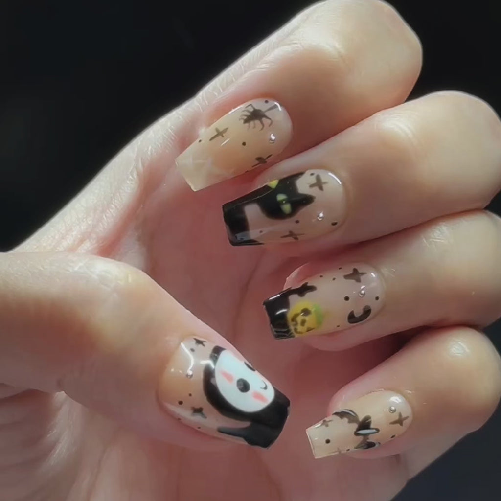 Hand wearing EyeCandys Trick or Chic Press-On Nails with warm tan nails, black drip tips, Halloween characters, and spider web details