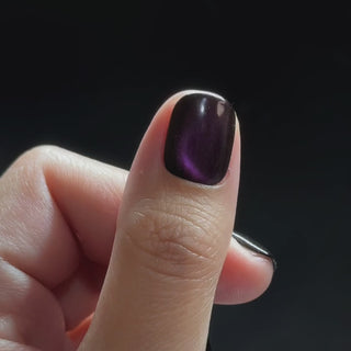 Hand wearing EyeCandys Nightshade Press-On Nails, featuring short round deep plum cat-eye nails with a warm violet-to-magenta shift and fine sparkle.
