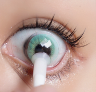Eyecandys Libre Green contact lens sliding onto an eyeball with a dark iris of an Asian model