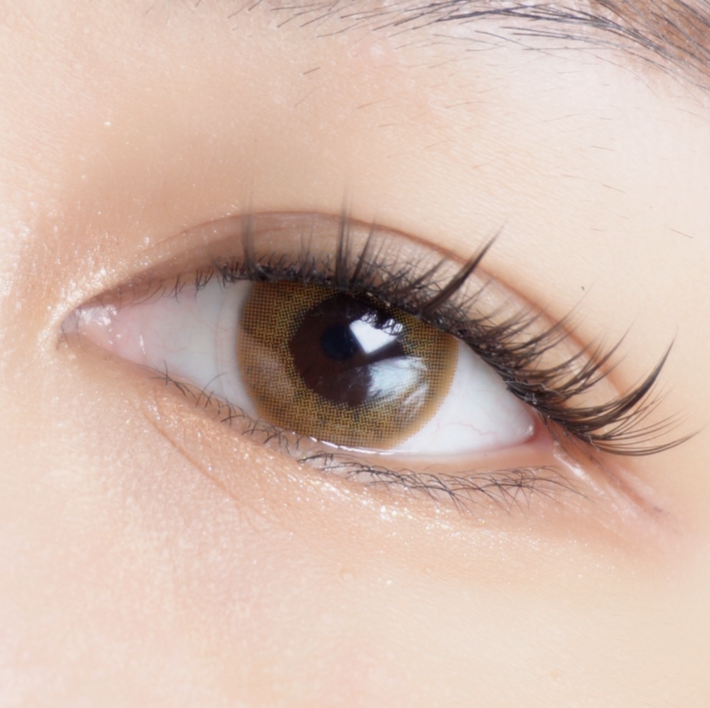 Eyecandys Libre Brown contact lens sliding onto an eyeball with a dark iris of an Asian model