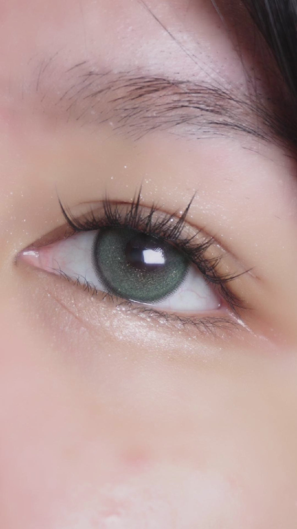 Model putting on the Winkly Green colored contacts on naturally dark eyes, showing the natural enlarging effect of the prescription circle lens, paired with simple lash extensions.
