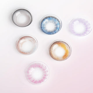 Various color contact lenses in blue, grey, violet, brown and pink, photographed on a pink background