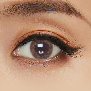 Close-up shot of model's eye adorned with Truffle Brown colored contacts for astigmatism, complemented by clean eye makeup, showing the brightening effect of the brown contact lens on dark brown eyes.