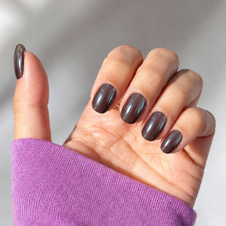 Hand wearing EyeCandys Vino Tinto Press-On Nails in pearlescent vino-tinto burgundy with a garnet metallic glow, featuring elegant press on nails short in an oval shape for fall and winter.