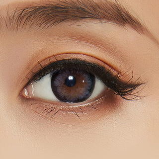 A close-up image capturing the intricacies of the model's eye, accentuated by the Pink Label Blossom Grey contact lens and accompanied by peach-colored eyeshadow.