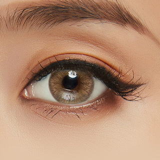 Close-up shot of model's eye adorned with Eyelighter Brown colored contacts for astigmatism, complemented by clean eye makeup, showing the brightening effect of the warm brown contact lens on dark brown eyes.