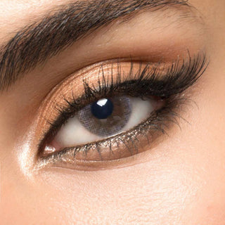 A blue circle contact lens on top of a brown eye with smoky eye makeup and long eyelashes.