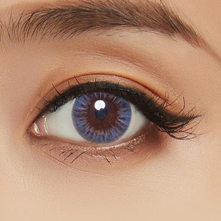 Close-up of female eye adorned with Birthday Blue contact lens complemented by peach eyeshadow.