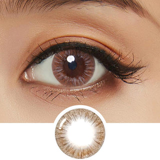 Close-up photo displaying the Birthday Brown contact lens on a white background, featuring a model with dark brown eyes and subtle natural eye makeup. The image also includes a cutout of the contact lens