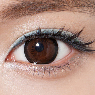 Close-up image featuring a model wearing Pink Label Bambi Almond Brown contact lens over dark brown irises, accompanied by subtle makeup