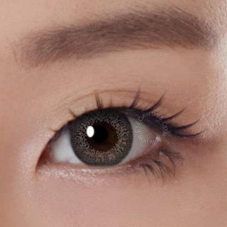 Close-up shot of a model eye wearing Lacelle Colors Frozen Grey colored contact lens in one eye that is naturally dark-brown with natural eye make up and long lashes